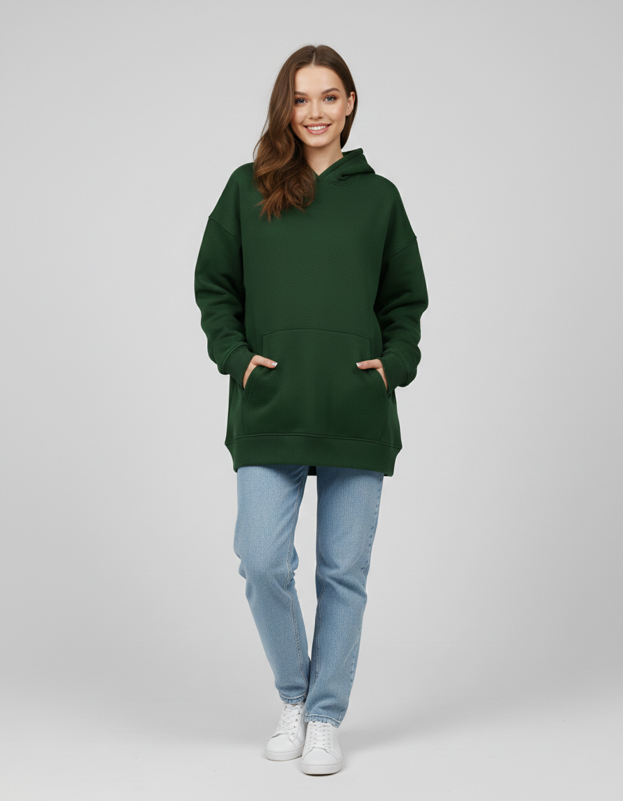 Woman in oversized green hoodie with kangaroo pocket, light blue jeans, and white sneakers