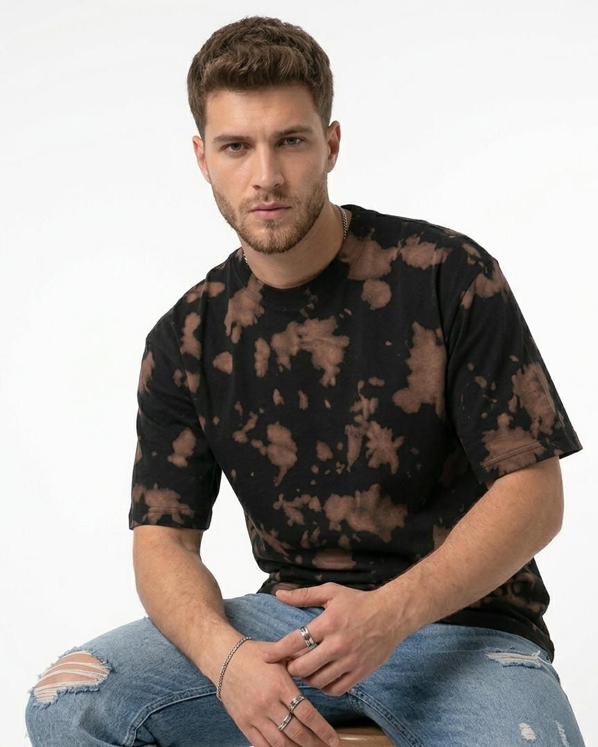 Man wearing black and brown tie-dye t-shirt and ripped jeans against white background