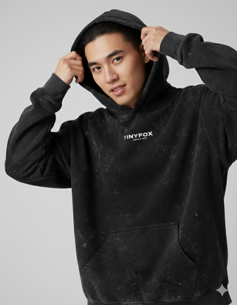 Man wearing a black acid wash hoodie with front pouch and minimal white text detail.