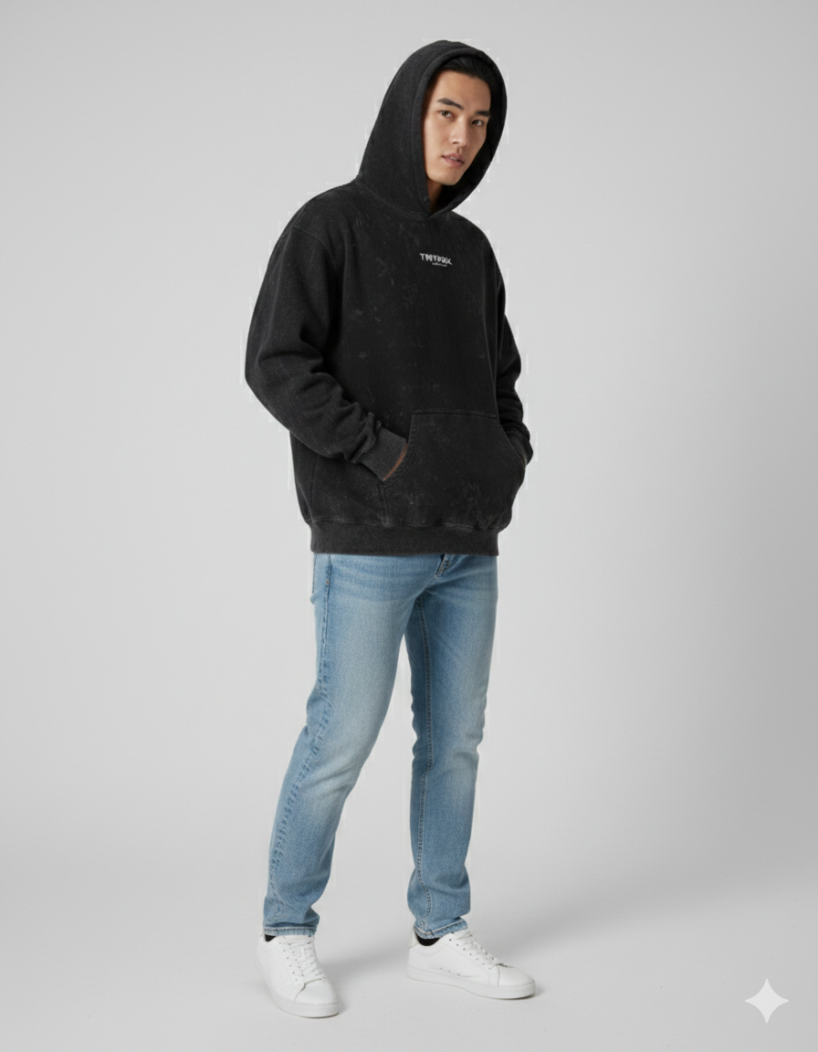 Man wearing black acid wash hoodie with hood up, light blue jeans, and white sneakers
