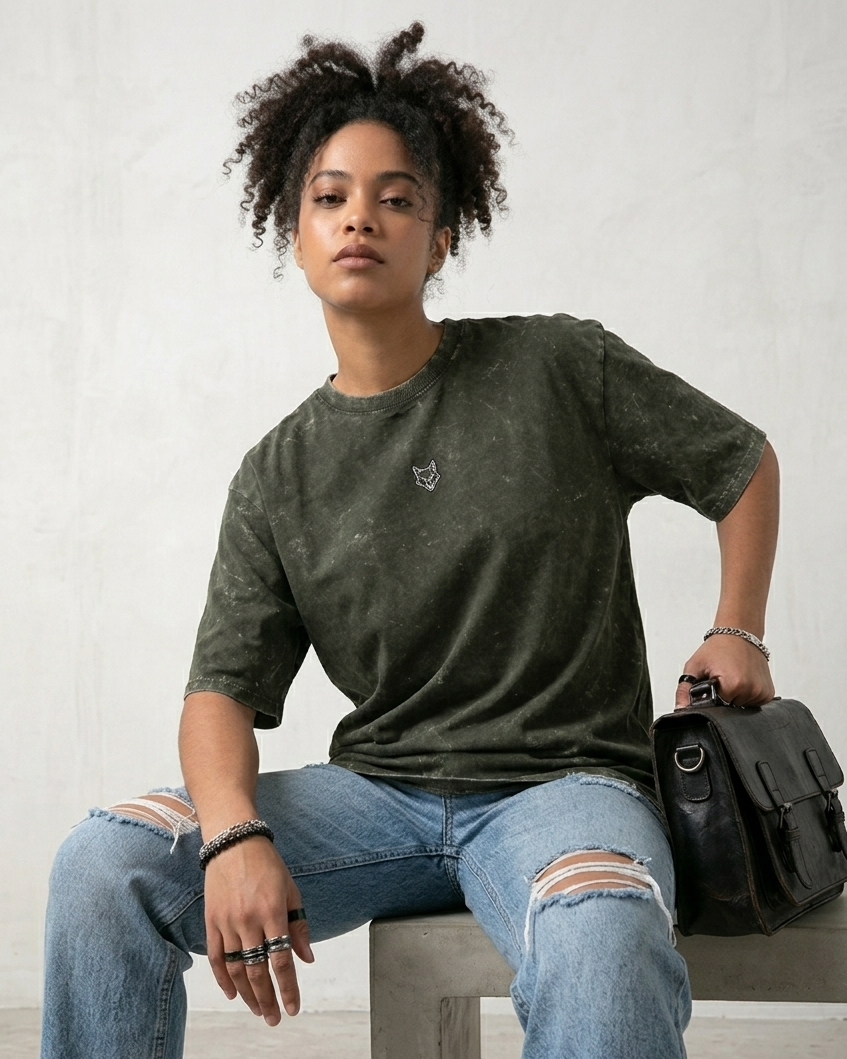 Woman in a washed green fox logo t-shirt and ripped jeans holding a black leather bag
