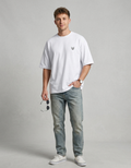 Man wearing white t-shirt with small fox head graphic, blue jeans, and white sneakers