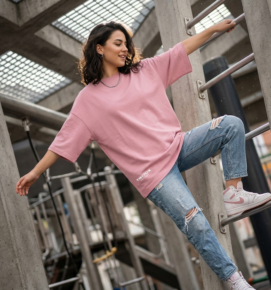 Woman wearing oversized pink t-shirt and ripped jeans climbing outdoor metal bars